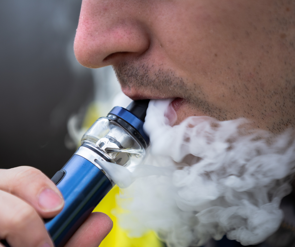 Man vaping with a blue e cigarette exhaling thick grey, white vapour.