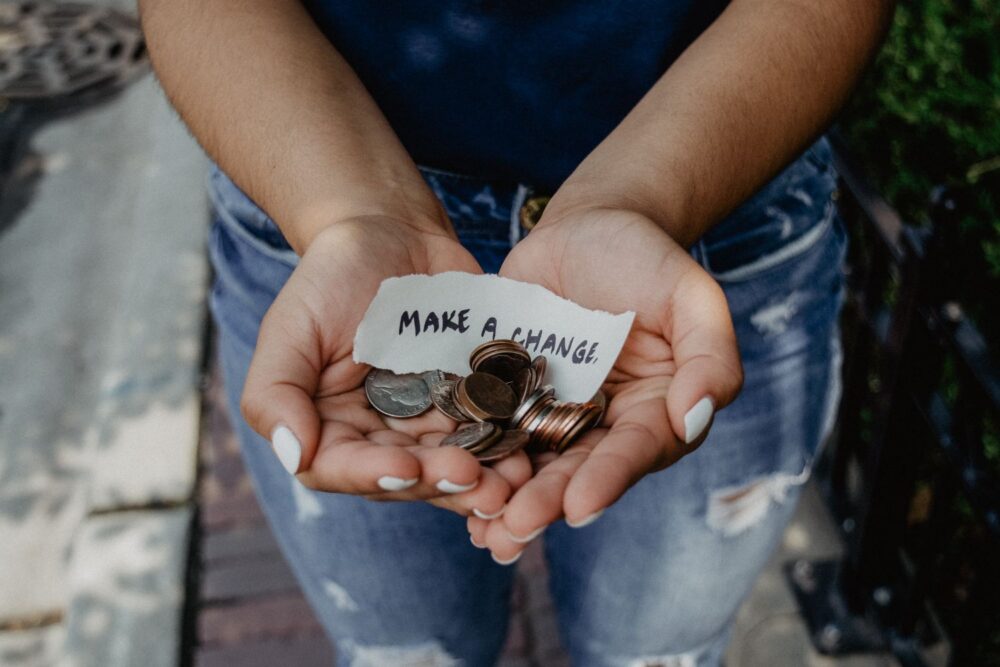 close up image of a persons cupped hands holdind a selection of coins and a scrap of paper with 