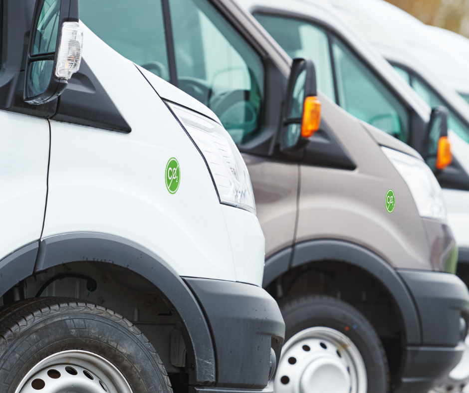 Close-up of three commercial vans parked in a row, each displaying a green circular CO2 emission sticker on the front side panel.