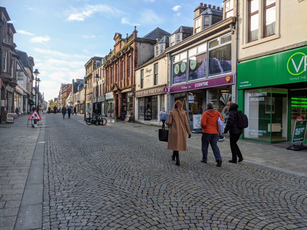 Three people walking down a pedestrianised street in Fort William