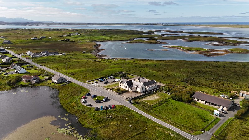 Aerial view of a rural island village with scattered houses, green fields, and winding waterways under a partly cloudy sky.