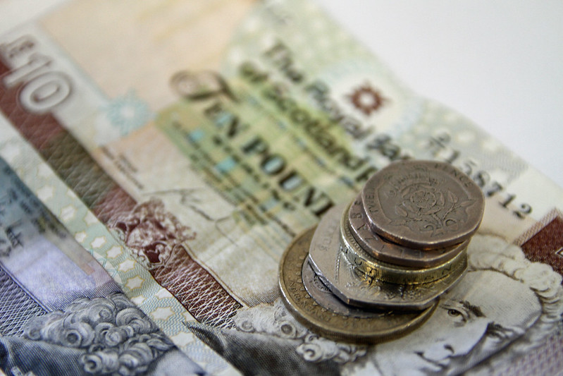 Stack of coins placed on top of a ten-pound banknote.
