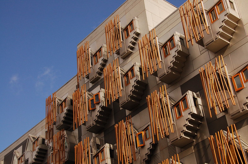 Modern building facade with protruding balconies and vertical wooden slats against a clear blue sky.