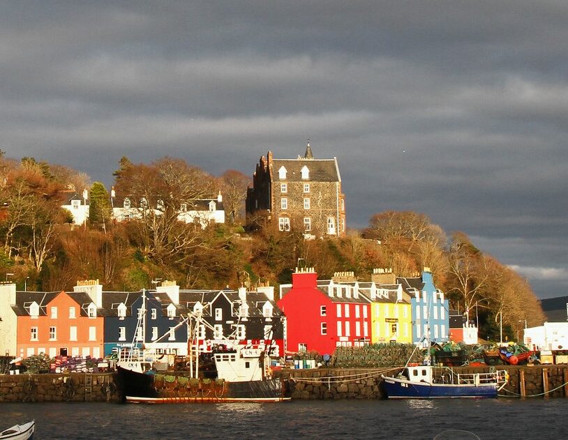 Brightly coloured island houses around a harbour under a cloudy sky.