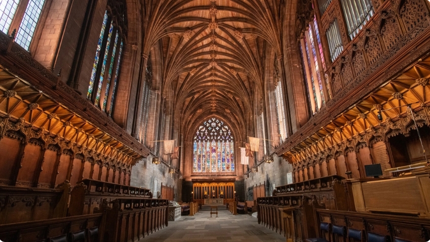 Spacious church interior featuring high arched ceilings, stained glass windows, and rows of ornate wooden seating.